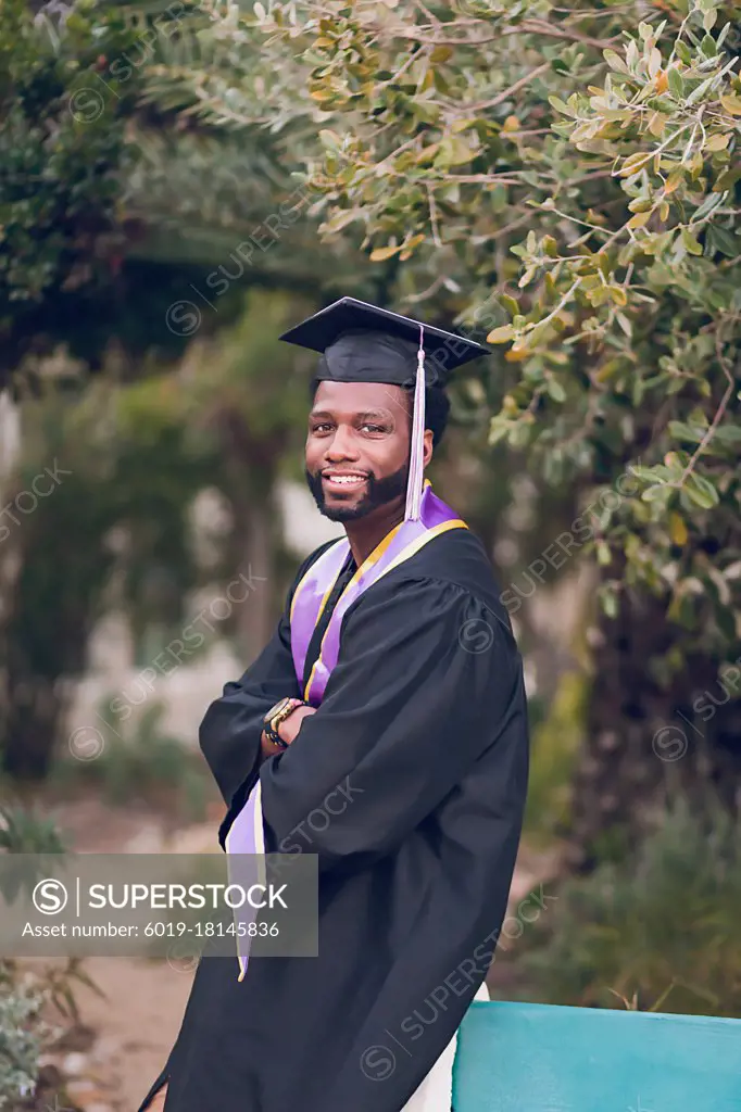 Young man with arms crossed wearing a graduation gown/cap.