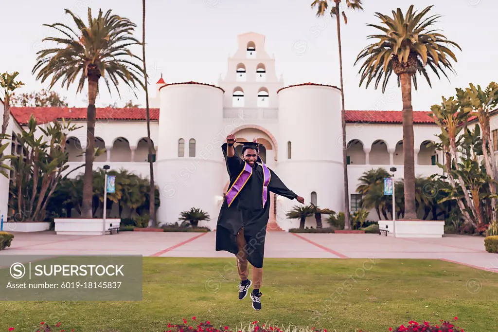 Man jumping, wearing a graduation gown/cap.