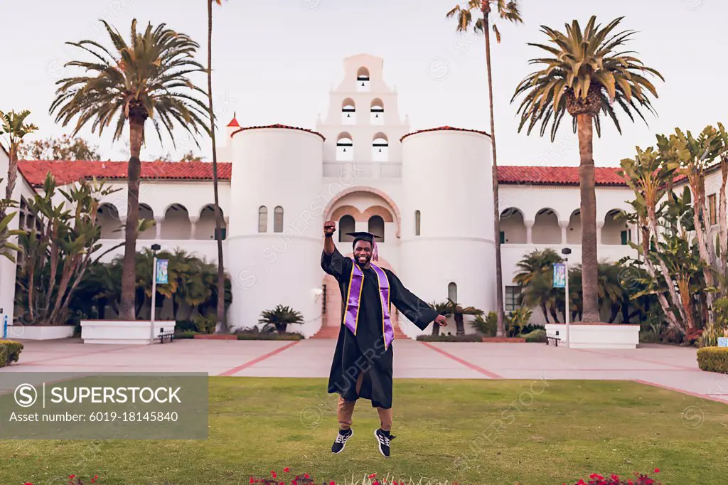 Man jumping, wearing a graduation gown/cap at the University.