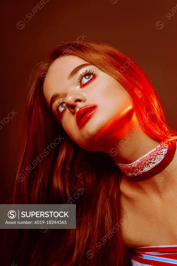 Close-up portrait of beautiful red-haired green-eyed girl with dark trendy makeup: red lips and red eyeshadows, with choker at her neck. Gloomy and sad portrait