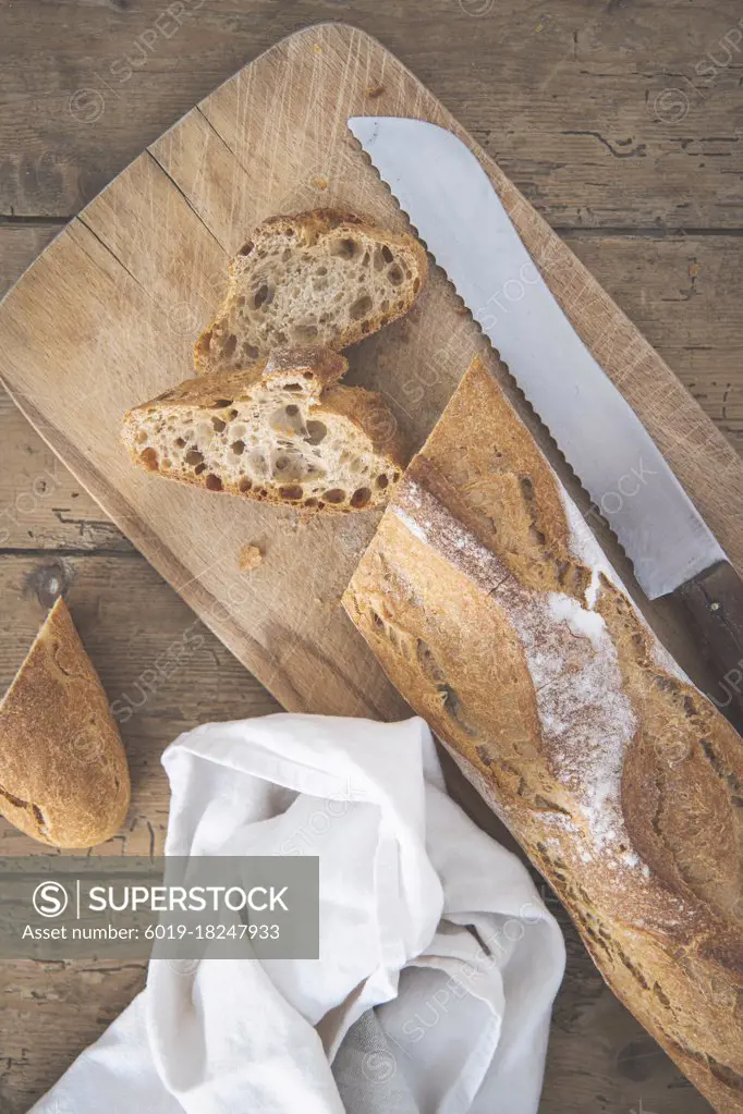 A baguette is cut on a cutting board with a knife