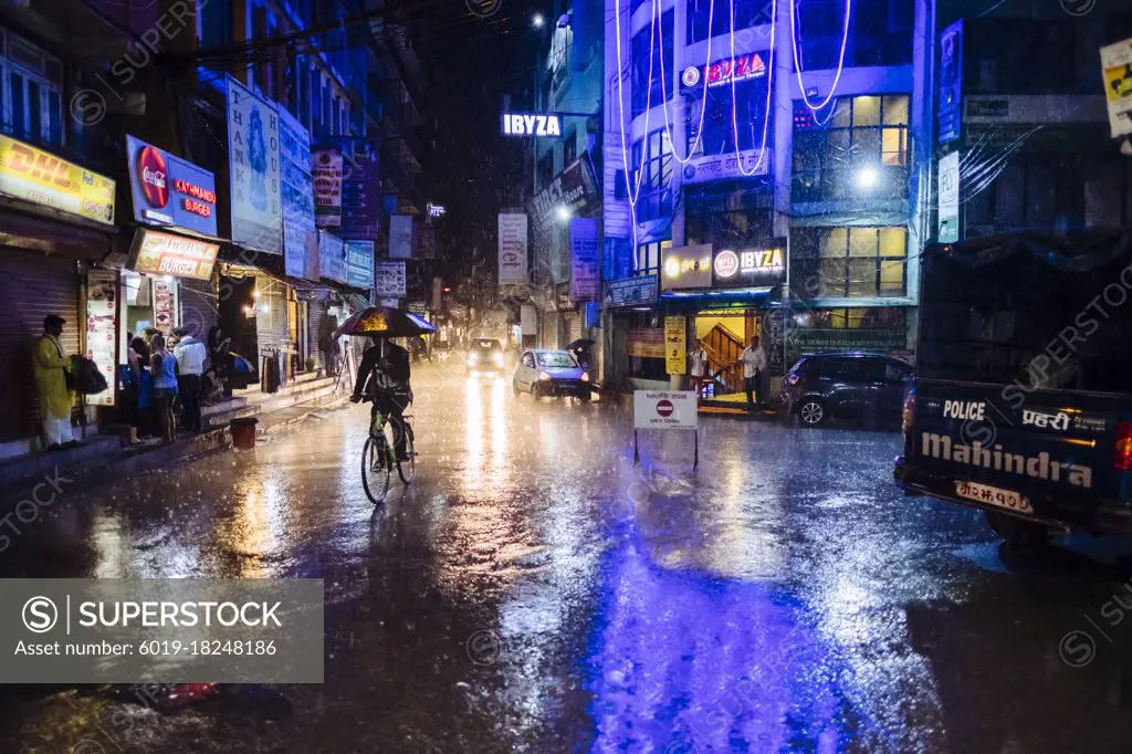 Nepali man cycling in Kathmandu main streets of Thamel during heavy monsoon rain at night time in Nepal.