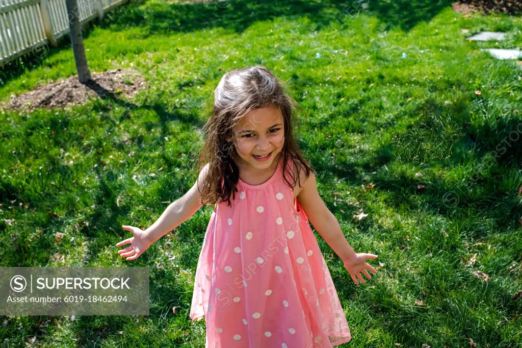 Young girl in pink dress smiling outside in yard
