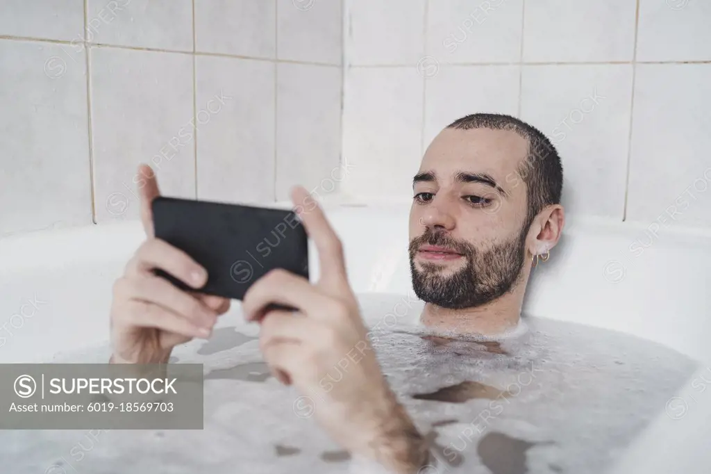 Smiling white man relaxing in the water watching black mobile phone