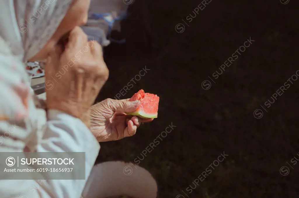 Old woman eats juicy red watermelon in sunlight, copy space