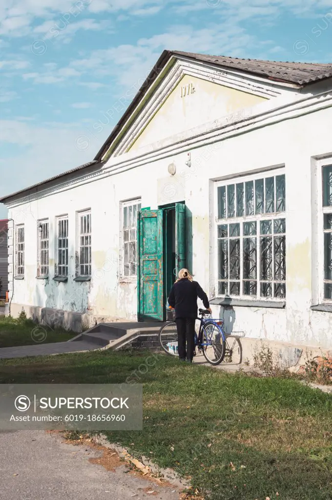 Woman gets on bicycle next to old peeling vintage building of 1971