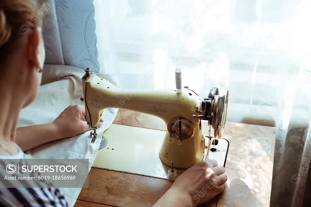 Woman sews on old retro sewing machine at home