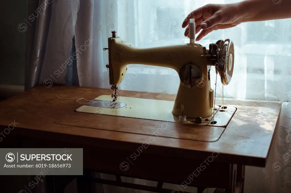 Hand takes spool of thread from old retro sewing machine