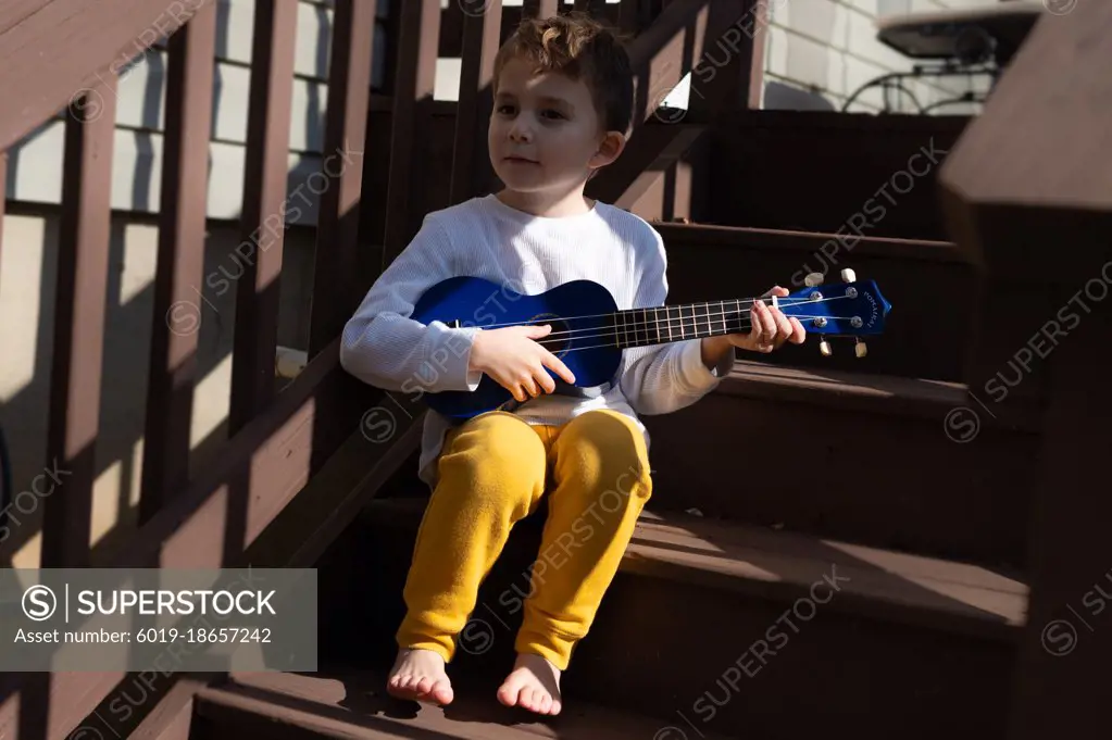 Little boy playing a blue ukulele on the back steps