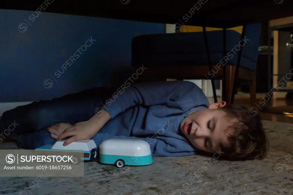 Boy playing with toy car under the coffee table on the living room rug