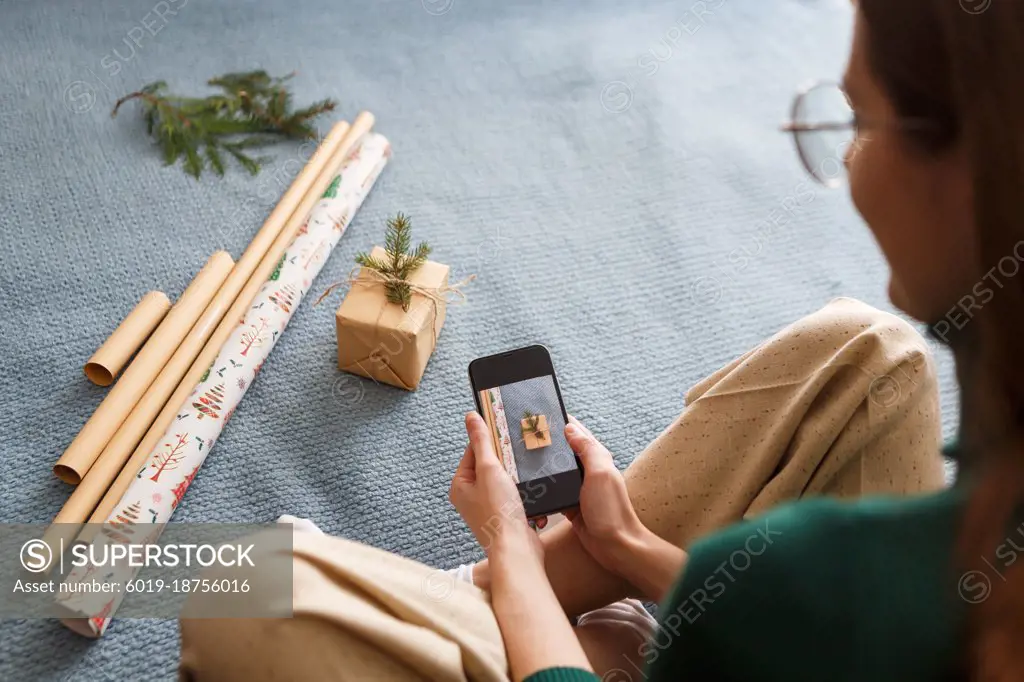 Young woman takes pictures of freshly wrapped Christmas presents