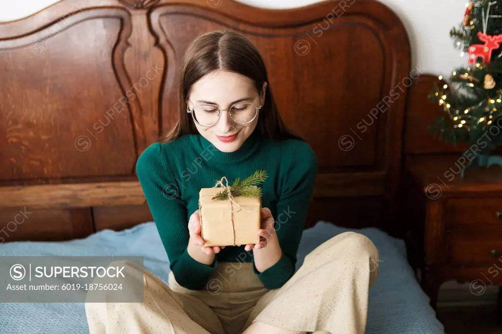 Young woman with a Christmas wrapped gift sitting on the bed