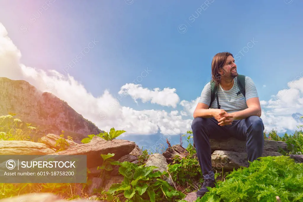 Young man sit in beautiful mountains on hiking trip.