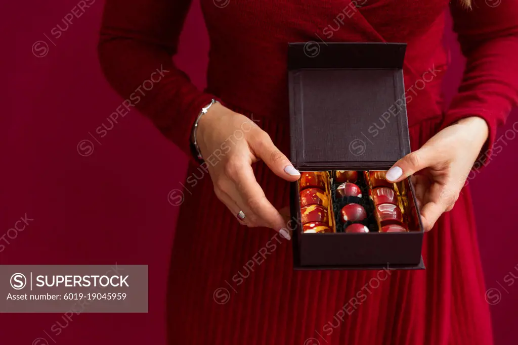Female holding bonbon in box on red background