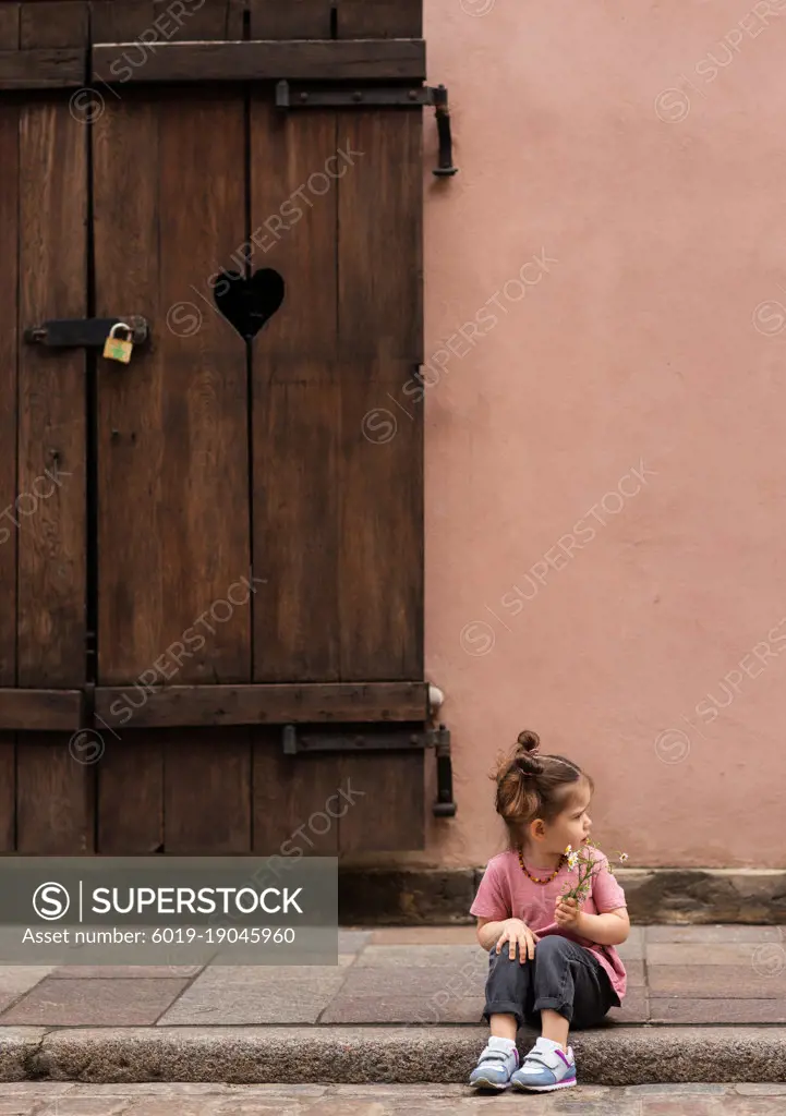 Little cute toddler girl sitting on road at Old town