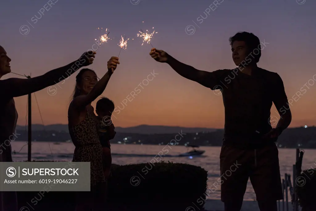Silhouette of group of friends having with bengal lights at dusk