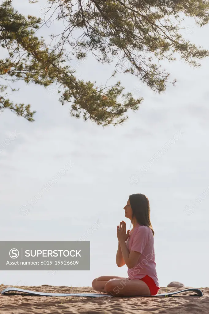 A woman in a lotus position meditates on the beach under the pines.