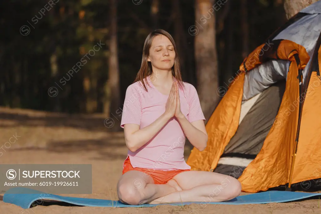 A traveler in a lotus position near tents in a pine forest.