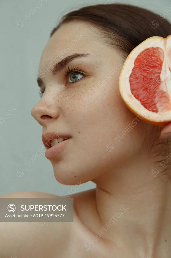 Close-up portrait of a young woman with freckles and half a grapefruit