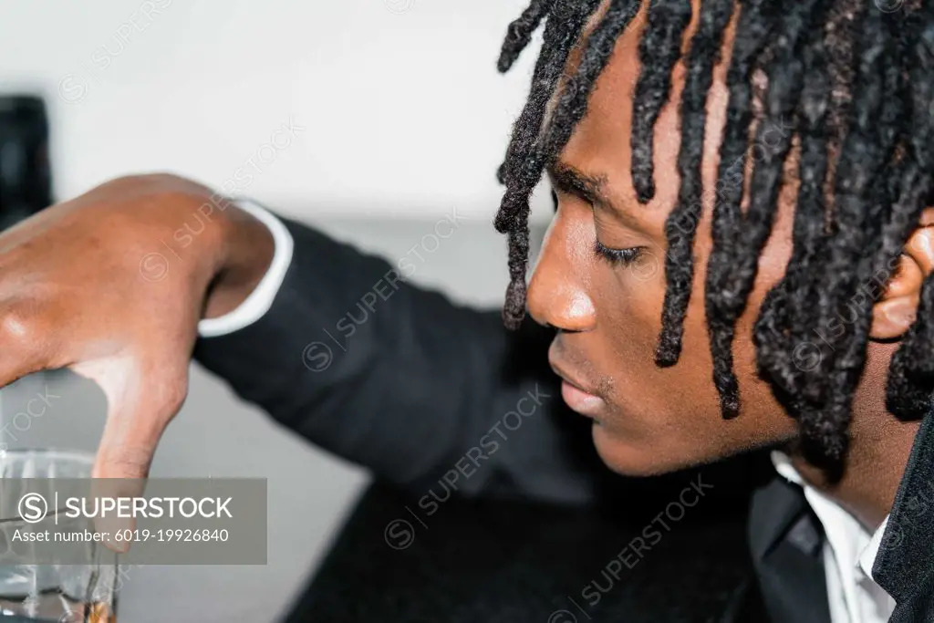 Black man with dreadlocks wearing a suit having a drink
