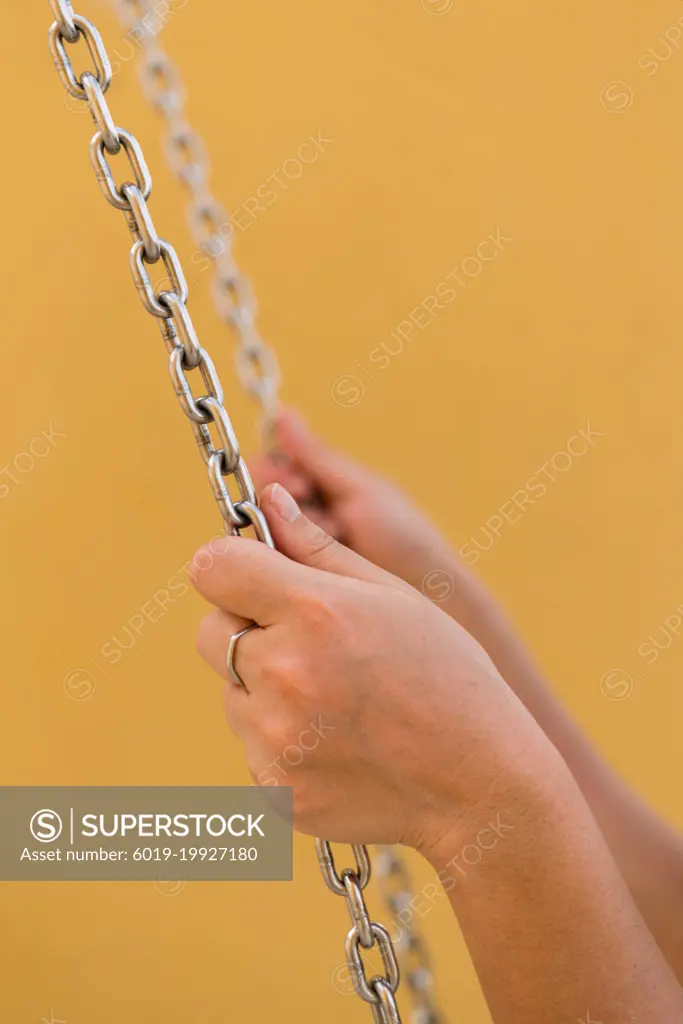Hands holding swing chain on a yellow background