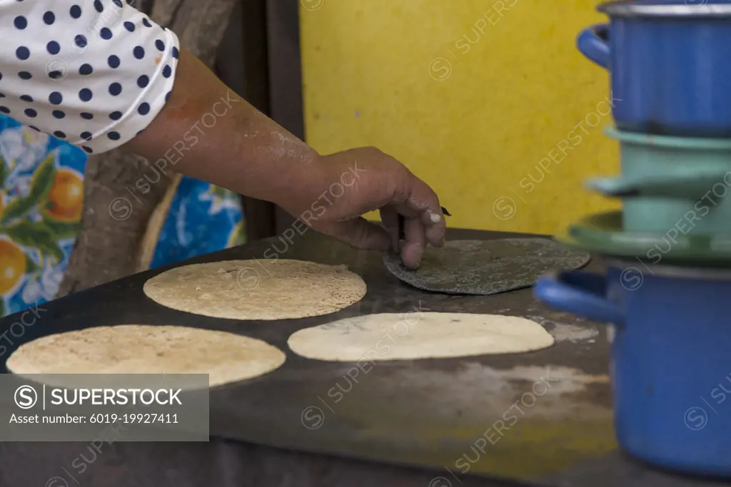 Mexican woman preparing cooking some tortillas on a firewood griddle