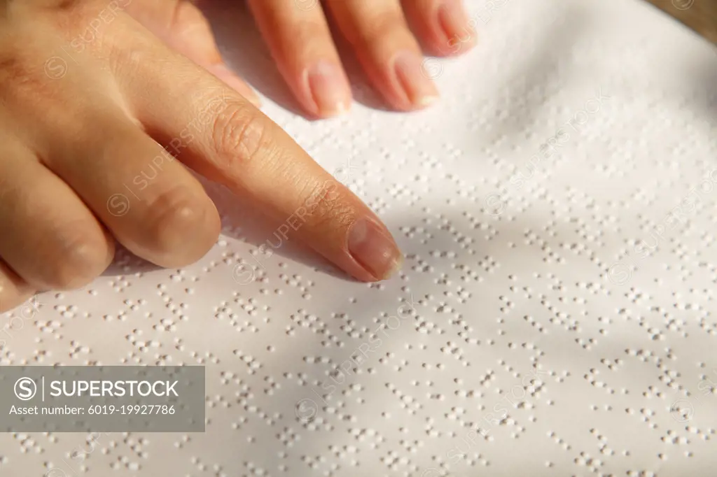 Woman's hand on a book page with braille. Female finger