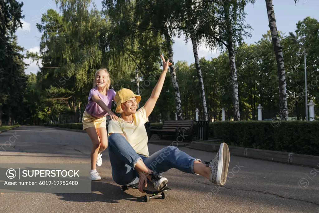 Cheerful girl and mother playing with skateboard in the park.