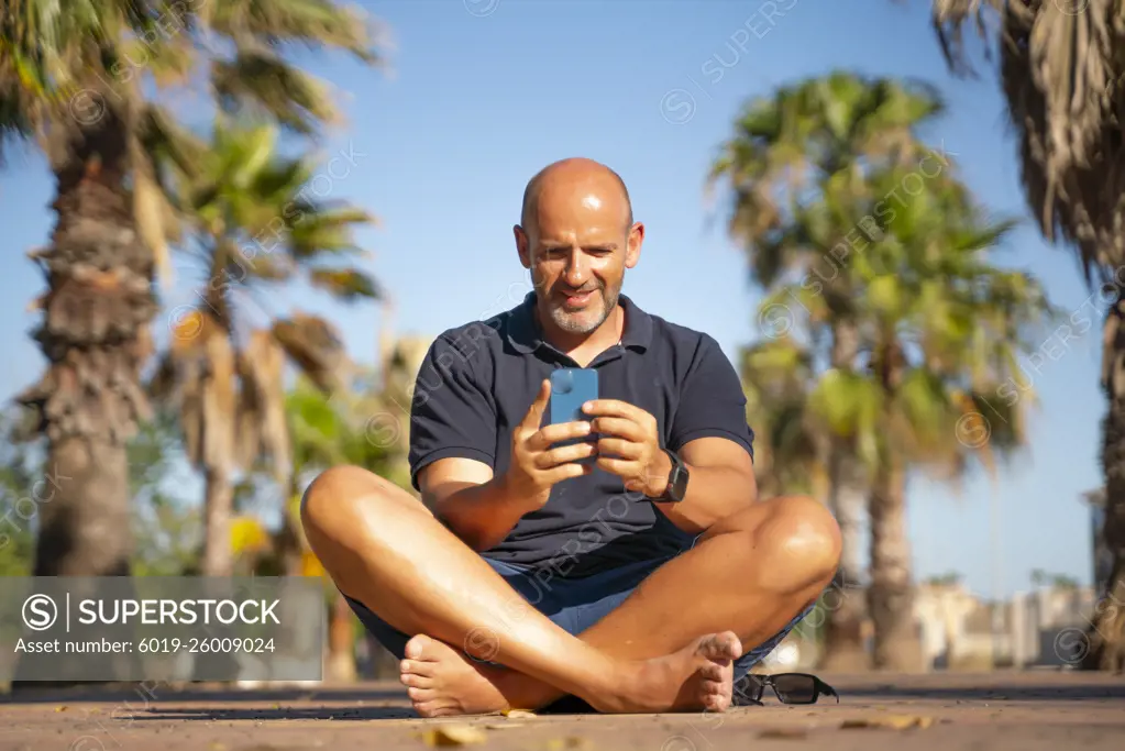 Bald man talking and using his smartphone in a tropical country