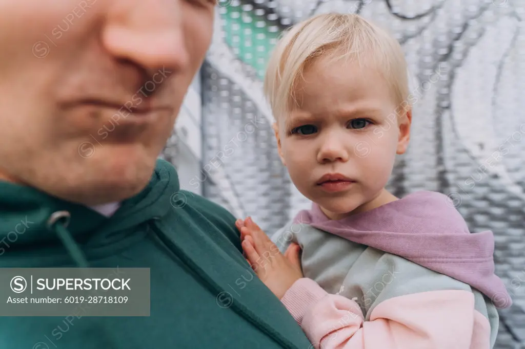 Dad holding two-year-old daughter in arms with a serious expression