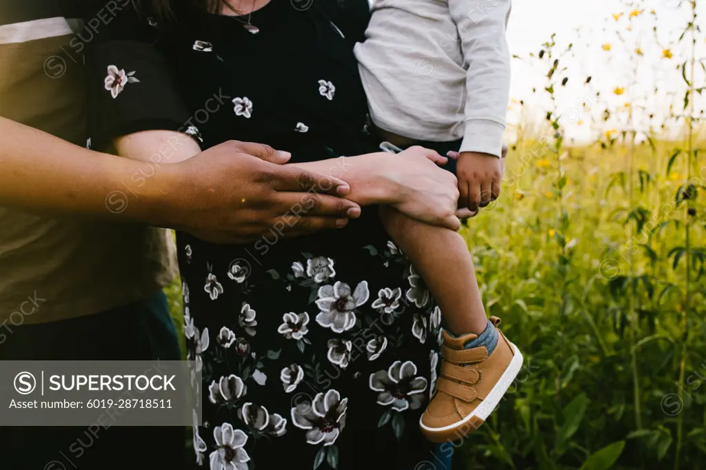 Pregnant mom holds toddler with dad in outdoor flower field