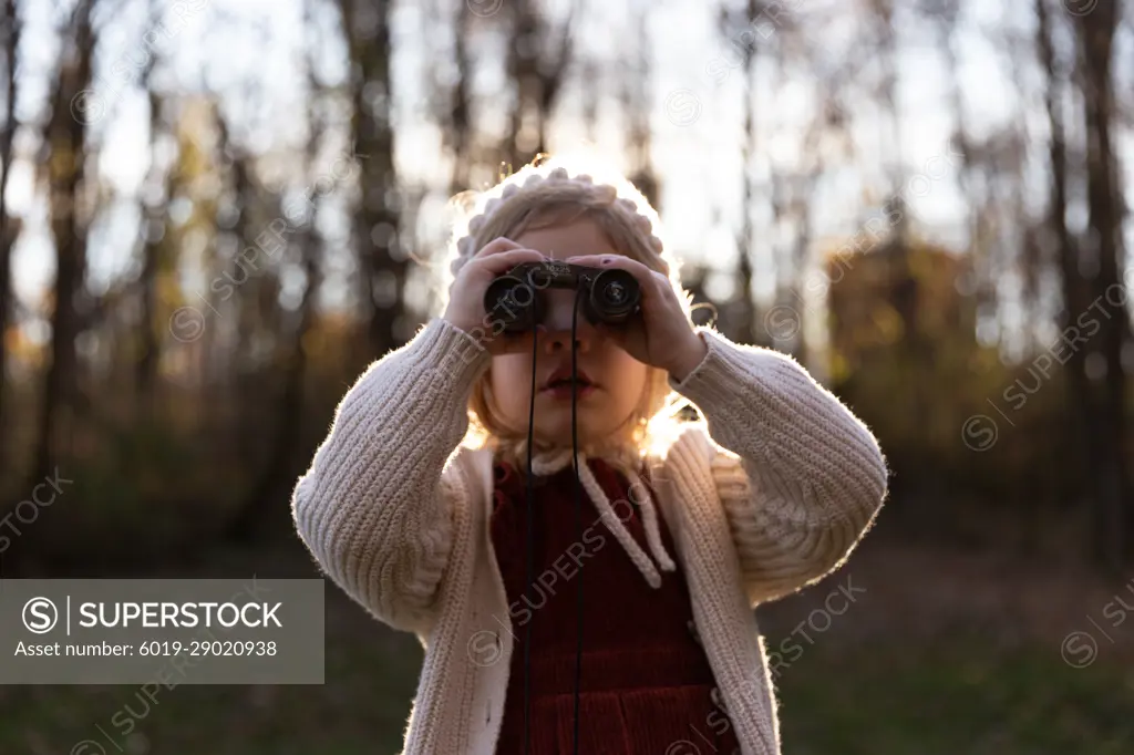 A young girl looks through binoculars while on a hike