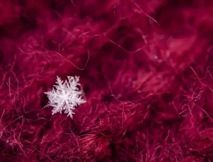 Close up of snowflake against a red woolen background.
