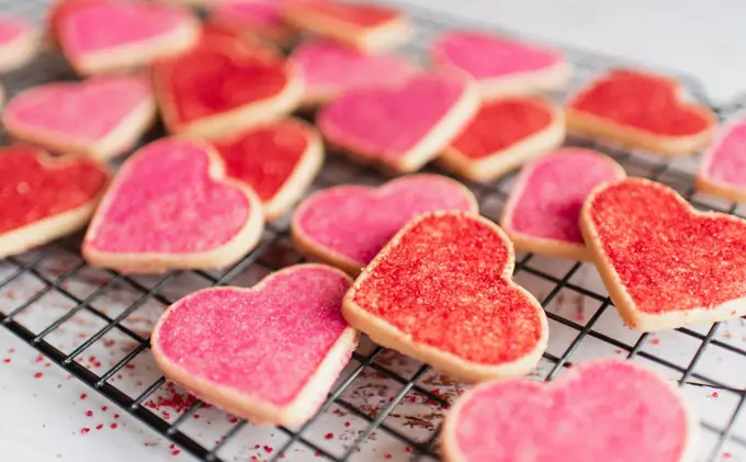 Close up of many decorated heart shaped cookies on cooling rack.