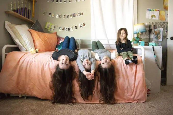 Four happy sisters with long hair laying on a bed together.