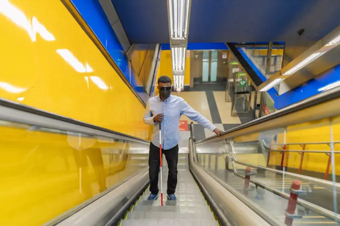 young blind african man climbing the escalator