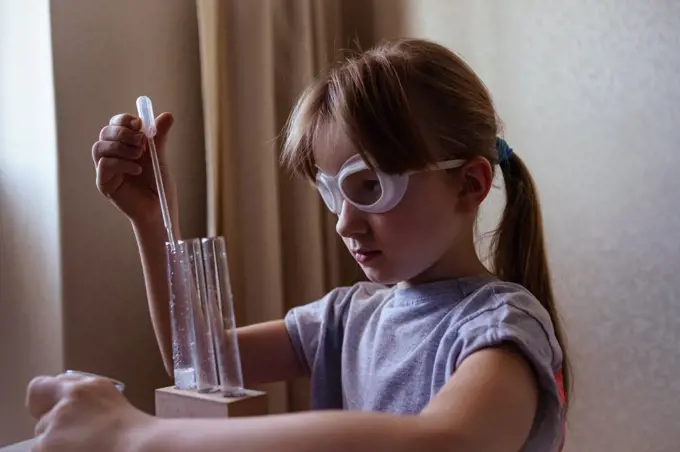 a girl in goggles conducts chemical experiments at home