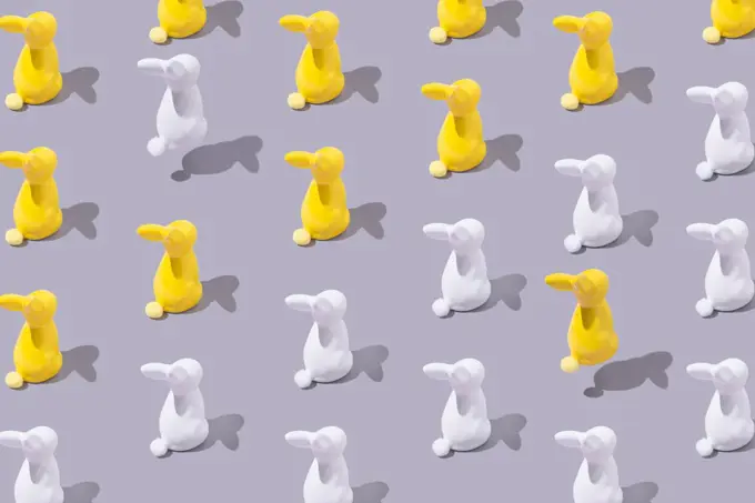Creative pattern with yellow and white plastic bunny on grey bac