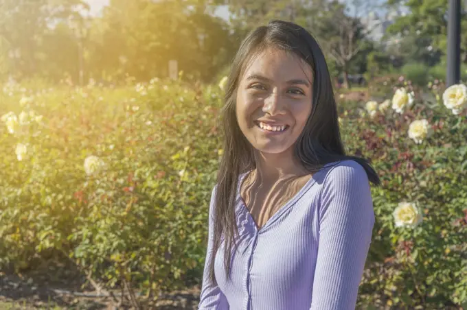 Young smiling Latin woman in a park full of roses.
