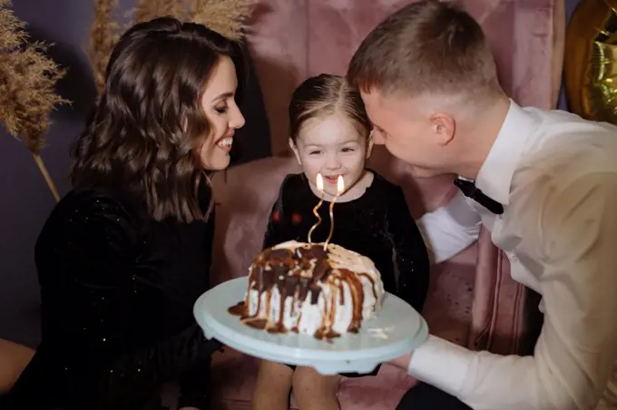 Little girl blows out the candles on the cake with her parents