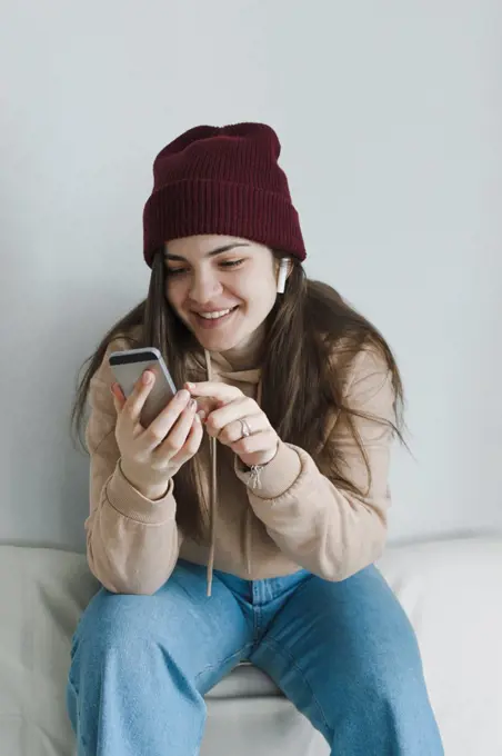 Stylish young woman smiling, using phone, listening to music.