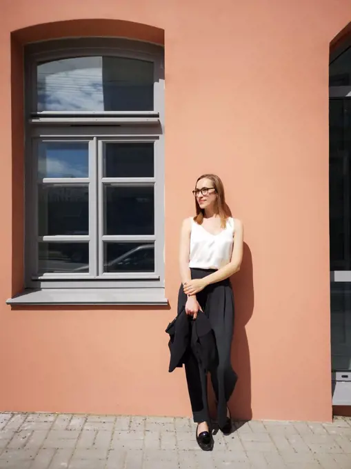A young woman with full-length glasses in front of the wall and window