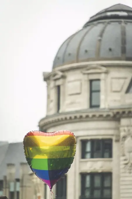 A heart shaped rainbow balloon floats in front of a building
