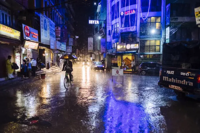 Nepali man cycling in Kathmandu main streets of Thamel during heavy monsoon rain at night time in Nepal.