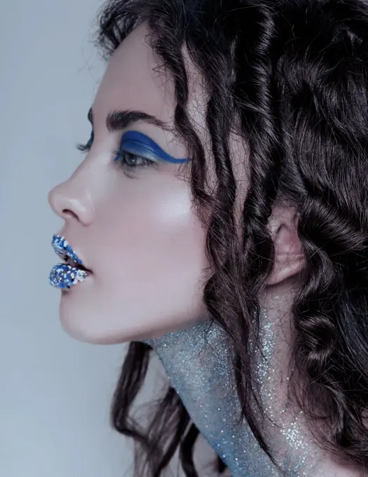 Beautiful brunette mermaid woman with creative blue and glitter make up and jewelry on her wet hairstyled head, bushy eyebrows.