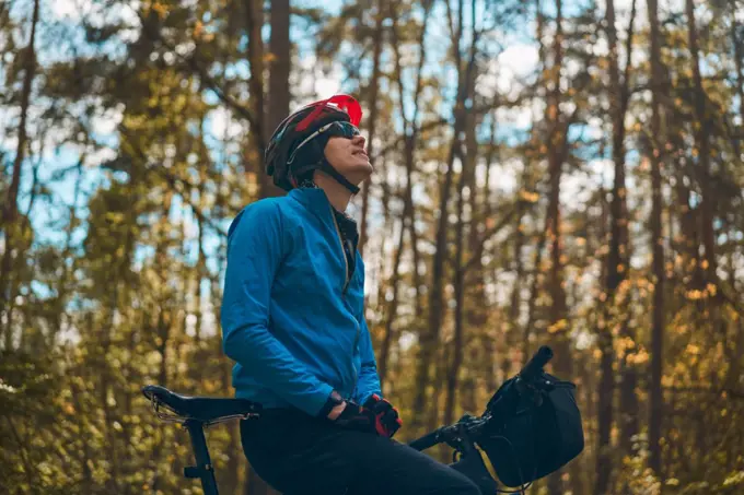 Man wearing bicycle helmet standing in forest, spending free vacation time on a bicycle trip in a forest.