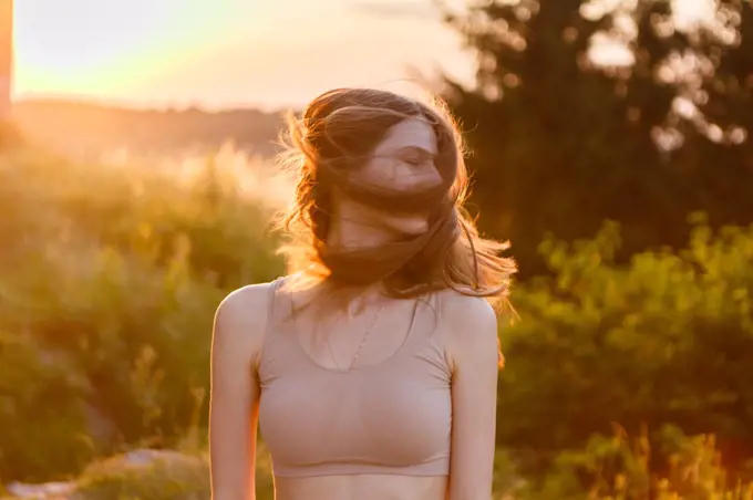 young woman joyfully waving her hair at sunset in the middle of nature
