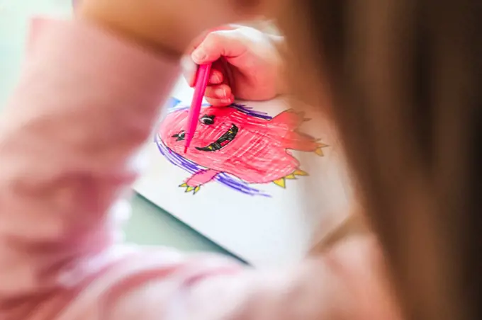 girl draws smiling pink monster with purple hair, look from under arm