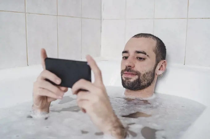 Smiling white man relaxing in the water watching black mobile phone