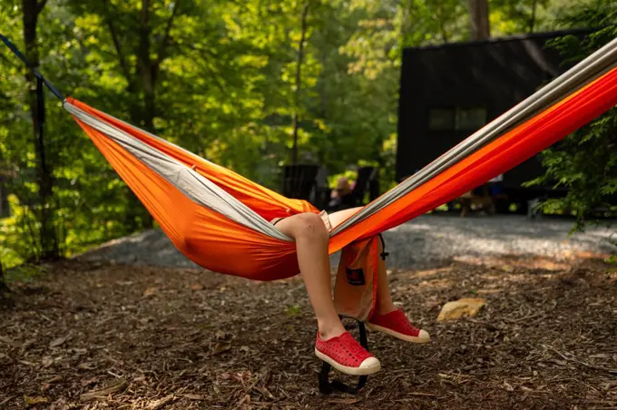 Legs of a little boy hanging from orange hammock at a campsite